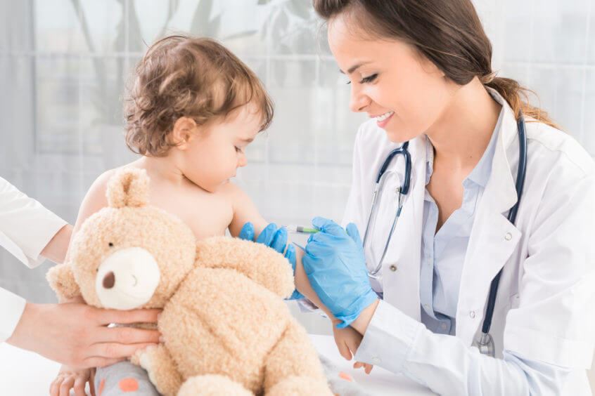 female doctor giving vaccine to a toddler holding a bear